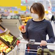 Young woman wearing disposable medical mask shopping in supermarket during coronavirus pneumonia outbreak.